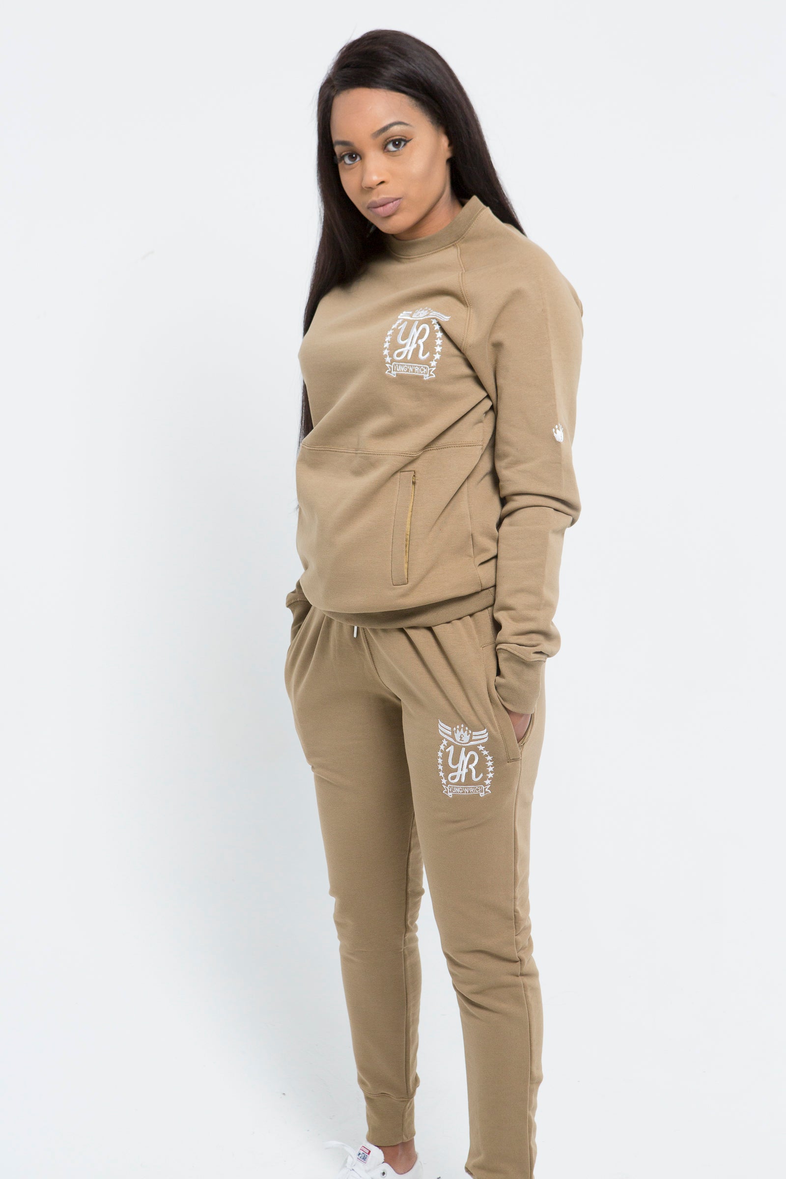 Yung'n'Rich beige crew neck tracksuit shown in standing pose, featuring white logo branding on chest and thigh, slim-fit design with tapered legs and ribbed cuffs, photographed against white background