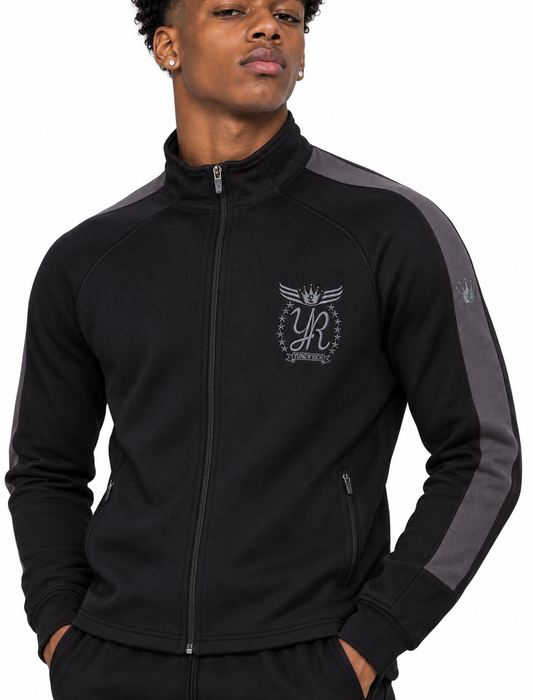 Jaden Brooks wearing the YUNG’N’RICH men’s grey and black tracksuit, front detail of the embroidered crest, zip and grey sleeve panel.