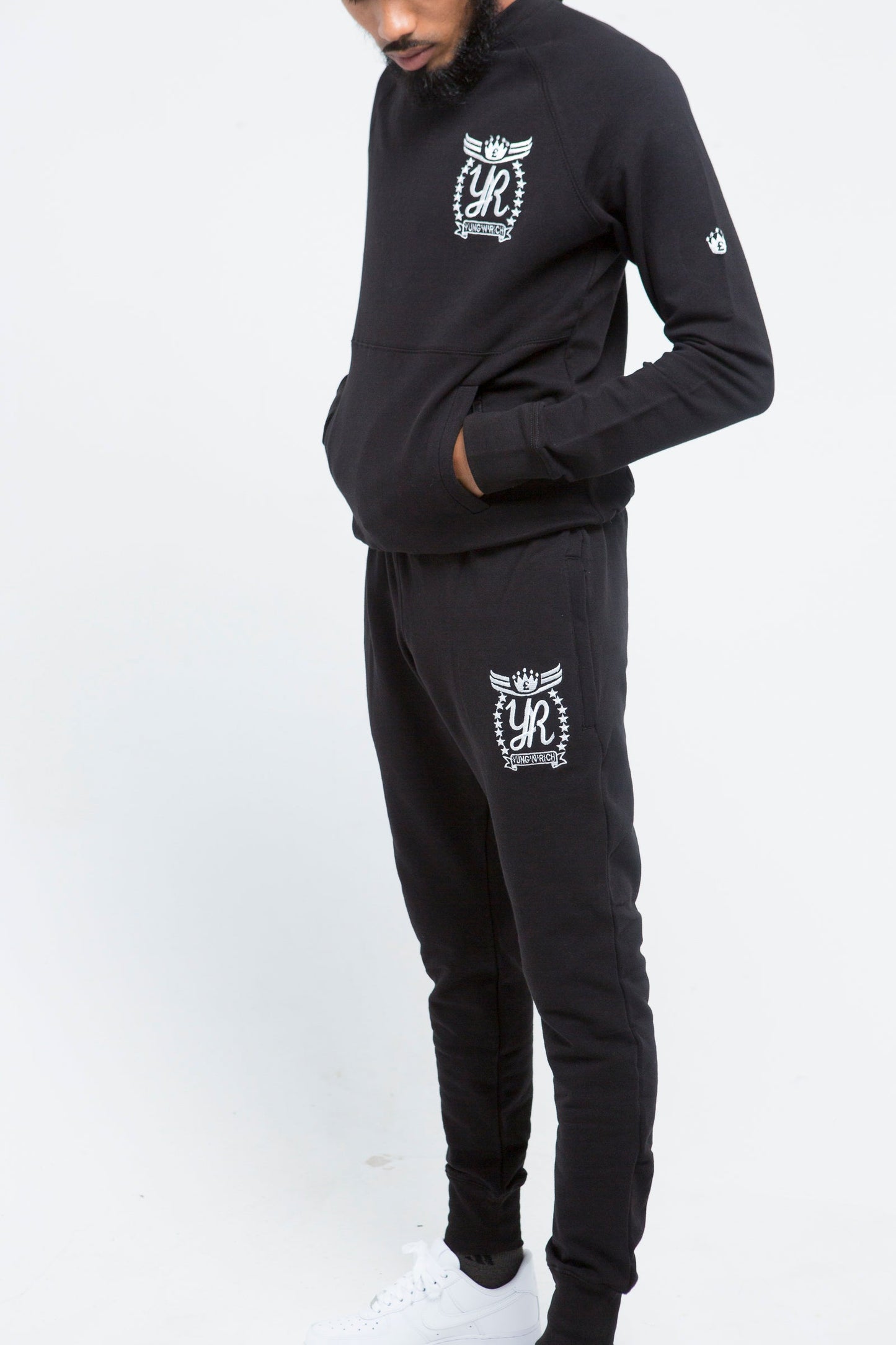 Yung'n'Rich black crew neck tracksuit detail shot on male model, highlighting white ornate logo branding and pocket details, close-up view of fabric texture and fit, photographed against white background