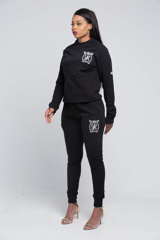 Yung'n'Rich black crew neck tracksuit shown in standing pose, featuring white logo branding on chest and thigh, slim-fit design with tapered legs and ribbed cuffs, styled with clear heels, photographed against white background